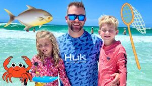 Family at the beach: father with two kids posing in the surf with cartoon sea creatures and a fishing net overlay nearby. coast and turquoise water in the background.
