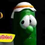 Green VeggieTales cucumber character with a white and orange headband on a black background, VeggieTales logo in the bottom-left corner.