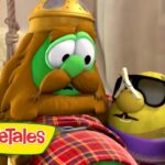 Two VeggieTales characters—a green cucumber with a Viking-style helmet and mustache, and a yellow pepper wearing sunglasses and a purple scarf—tied to ropes on a set, VeggieTales logo visible.