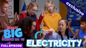 Adult presenter demonstrates a glowing electrical device to a group of diverse children in a classroom; thumbnail for an electricity episode of a science show.