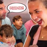 A man and two kids sit on a couch looking toward a laughing woman at right; a speech bubble says 'I SAID NO!' indicating a playful moment at a party.