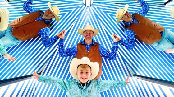 Group of five people dressed as cowboys with brown vests, blue shirts, and hats, standing under a blue-and-white striped canopy with arms outstretched.