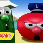 Green cucumber character with a white hat and surprised expression beside a red tomato character wearing a captain's hat on a beach, VeggieTales logo visible.