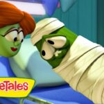 Green veggie dressed as a mummy leans in to kiss a red‑haired veggie; VeggieTales logo in bottom left.