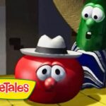 Red tomato character with a gray hat and surprised eyes sits on a yellow floor while a green cucumber in a striped robe looms behind in a VeggieTales scene, logo in the corner.