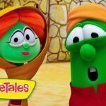Two VeggieTales characters converse outdoors, a green veggie with an orange hood on the left and a taller green veggie with an orange hat on the right, with a stone building behind them and the VeggieTales logo in the corner.