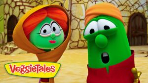 Two VeggieTales characters converse outdoors, a green veggie with an orange hood on the left and a taller green veggie with an orange hat on the right, with a stone building behind them and the VeggieTales logo in the corner.