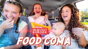 Four friends and a baby in a car, laughing as they eat burgers with an In-N-Out sign and 'Food Coma' text overlay.