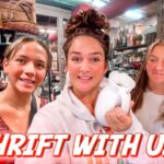Three friends in a cluttered thrift store; center holds a white vase, bottom text 'THRIFT WITH US!'