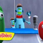 Larry the cucumber and a puzzled tomato stand on a VeggieTales set with a blue desk and robot host in the background.