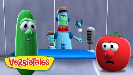 Larry the cucumber and a puzzled tomato stand on a VeggieTales set with a blue desk and robot host in the background.