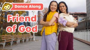 Two women stand with arms crossed on a urban walkway, a bold 'Dance Along' banner and 'Friend of God' text over the image, suggesting a video thumbnail.