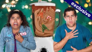 Two people look shocked beside a blender filled with chocolate swirl and holiday decorations (gingerbread, candy cane, Christmas tree) against a festive green background with an 'exclusive' banner.