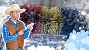 Man in a cowboy hat and brown leather vest points at a large colorful car-wash brush, with soap bubbles in the foreground.