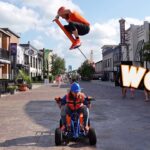 Child on a blue pedal go-kart rides toward the camera while another rider jumps a scooter high above them; large WOW graphic on the right.