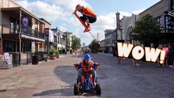 Child on a blue pedal go-kart rides toward the camera while another rider jumps a scooter high above them; large WOW graphic on the right.