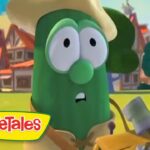 Green cucumber VeggieTales character wearing a straw hat, looking surprised in a sunny cartoon village setting.