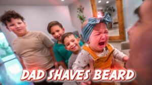 Crying baby in orange overalls held by an adult, while three older siblings gaze on; bold red text at the bottom reads 'DAD SHAVES BEARD'.