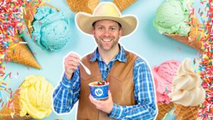 Smiling man in a plaid shirt and cowboy hat holding a blue cup of ice cream with a spoon, surrounded by colorful ice cream cones and scoops in a pastel background.