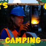 Camper in a blue helmet and orange safety vest holds a lit lantern in a dark forest, framed by a decorative 'Let's Go Camping' border.