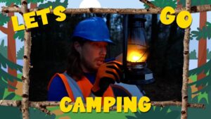 Camper in a blue helmet and orange safety vest holds a lit lantern in a dark forest, framed by a decorative 'Let's Go Camping' border.
