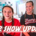 Two girls with braided hair sit in a bright bedroom, smiling at the camera with the bold 'OUR SHOW UPDATE!' text overlaid across the bottom area.
