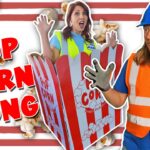 Thumbnail of a man in an orange safety vest and hard hat, a surprised woman in a safety vest, a giant popcorn box, and bold POP CORN SONG text.