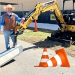 Construction site scene with a CAT excavator, a smiling worker in a hat and vest, an 'Under Construction' sign, and orange safety cones near a large golf-ball on a tee.