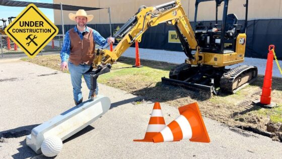 Construction site scene with a CAT excavator, a smiling worker in a hat and vest, an 'Under Construction' sign, and orange safety cones near a large golf-ball on a tee.