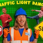 Bright kids’ video thumbnail with a smiling man in a hard hat and safety vest, STOP and SLOW signs, traffic lights, and a green background; “Traffic Light Dance” implied.
