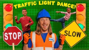 Bright kids’ video thumbnail with a smiling man in a hard hat and safety vest, STOP and SLOW signs, traffic lights, and a green background; “Traffic Light Dance” implied.