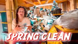 Woman gesturing in a cluttered basement full of boxes and junk, with a bold 'SPRING CLEAN' banner across the bottom.