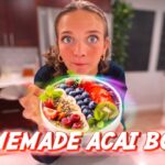 Woman in a kitchen presenting a colorful acai bowl topped with berries and mint; bold 'Homemade Acai Bowl' caption across the image.