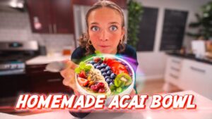 Woman in a kitchen presenting a colorful acai bowl topped with berries and mint; bold 'Homemade Acai Bowl' caption across the image.