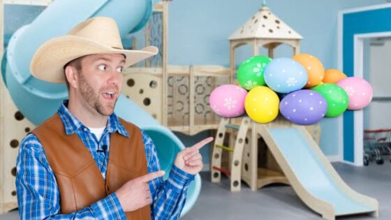 Man in a cowboy hat and brown vest points at a cluster of colorful Easter eggs indoors playground backdrop.