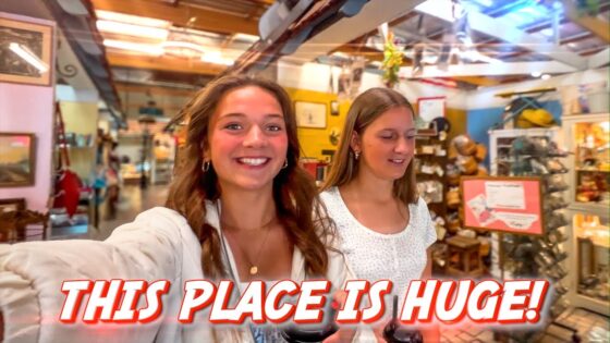 Two young women take a selfie in a busy, colorful gift shop with shelves full of items behind them.