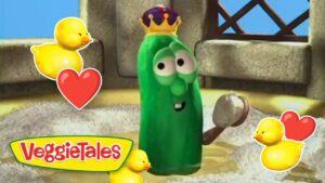 Green veggie character wearing a crown stands with ducklings and heart stickers in a sunny scene; VeggieTales branding shown bottom left.