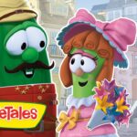 Green veggie character with a hat and mustache smiles at a pink-clad veggie holding a bouquet in a quaint town, VeggieTales logo visible.