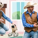 Two men dressed as cowboys in a child’s playroom, one pointing at a small pug-like plush beside metal bowls, the other holding a plastic dinosaur puppet.