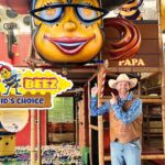Man in a cowboy hat and vest points at a colorful Billy Beez play area sign inside an indoor kids' attraction park.