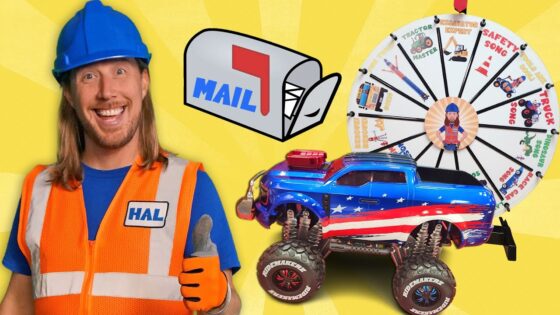 Smiling man in a blue hard hat and orange safety vest beside a red-white-blue toy truck and a prize wheel.