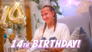 Girl with braided hair smiling at a birthday party, balloons in the background and a '14th Birthday!' overlay text.