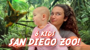 Woman with curly hair holding a baby in a pink sweater; lush jungle backdrop with an orangutan visible, and large red-and-white text '6 KIDS SAN DIEGO ZOO!' overlaid