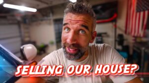 Man in a garage selfie with a surprised expression and a bold 'SELLING OUR HOUSE?' text overlay.