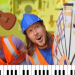 Two construction workers in orange safety vests lean toward a large prize wheel, a cartoon guitar sticker floating overhead, and a piano keyboard at the bottom edge for a playful scene.