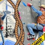 Two climbers in cowboy outfits scale an indoor rock wall; yellow DANGER tape frames the scene.
