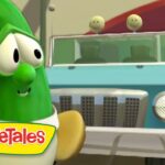 Larry the cucumber, a VeggieTales character, stands beside a light blue jeep in a sunny outdoor scene with the VeggieTales logo in the corner.