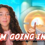 YouTuber with curly hair gestures toward a large MRI scanner, overlaid with the caption "I'M GOING IN!"