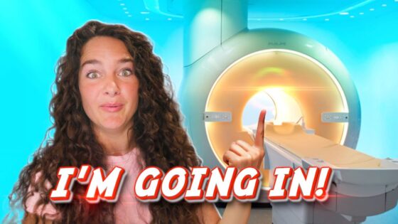 YouTuber with curly hair gestures toward a large MRI scanner, overlaid with the caption "I'M GOING IN!"