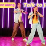 Two young dancers perform a joyful dance on a stage with purple neon vertical lights and 'Dance Along'/'Talk to Jesus' banners.